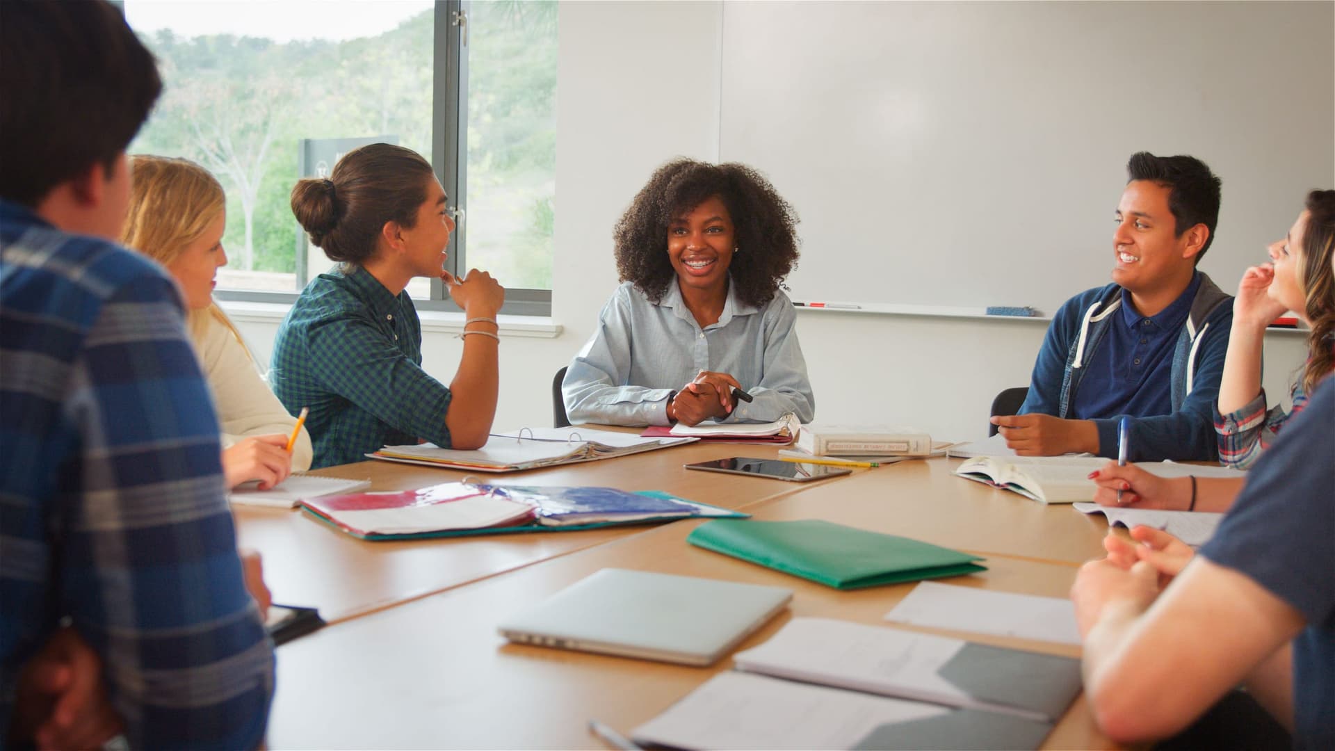 An educator sitting alongside a young student, supporting them through a classroom activity