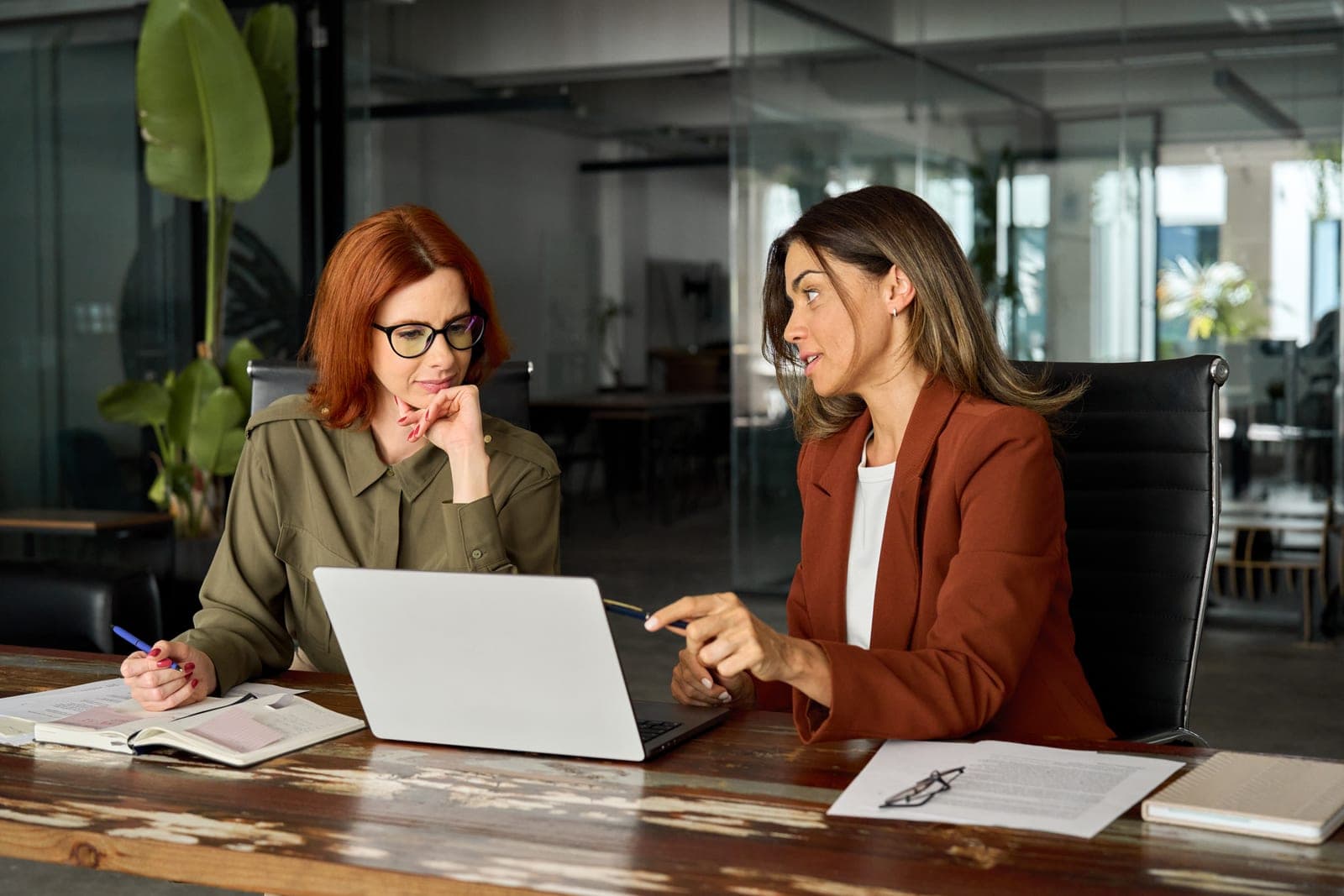 Board Certified Behavior Analyst leading a supervision meeting with a BCBA trainee, reviewing clinical documentation at a conference table
