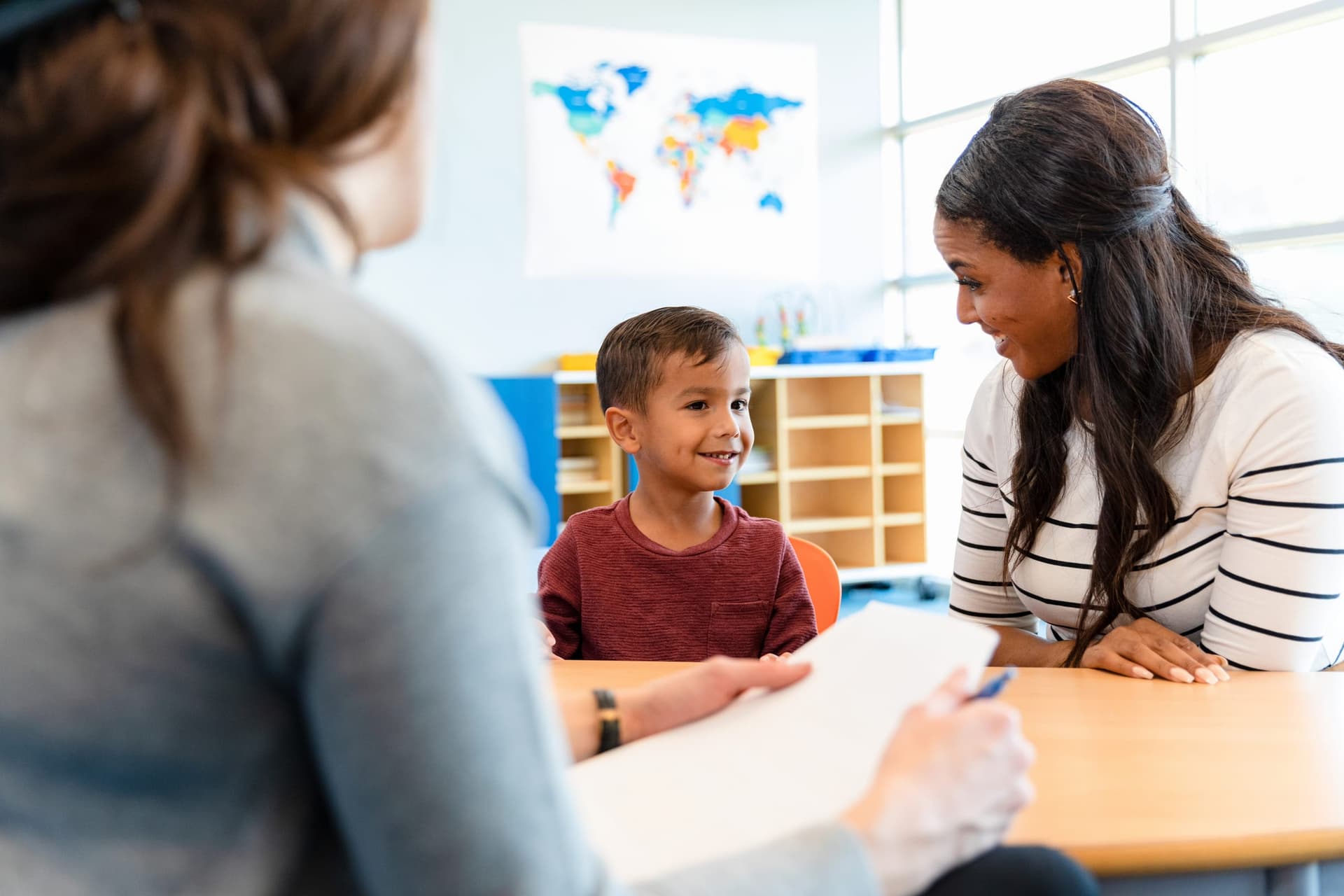 Niño sonriendo durante una sesión de ABA con su madre y terapeuta en un salón de clases
