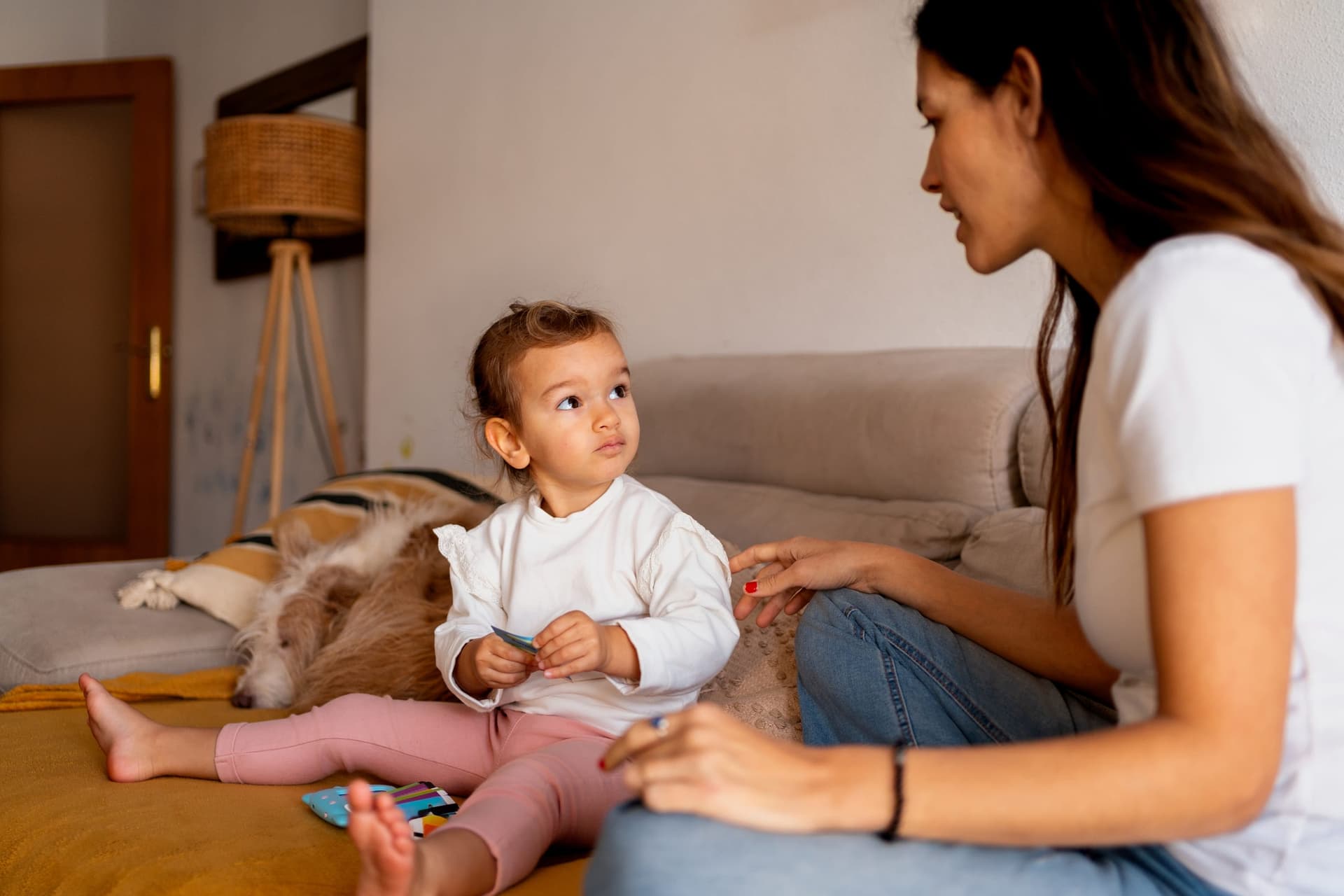 Mother sitting on a couch at home, talking with her toddler who is looking up at her