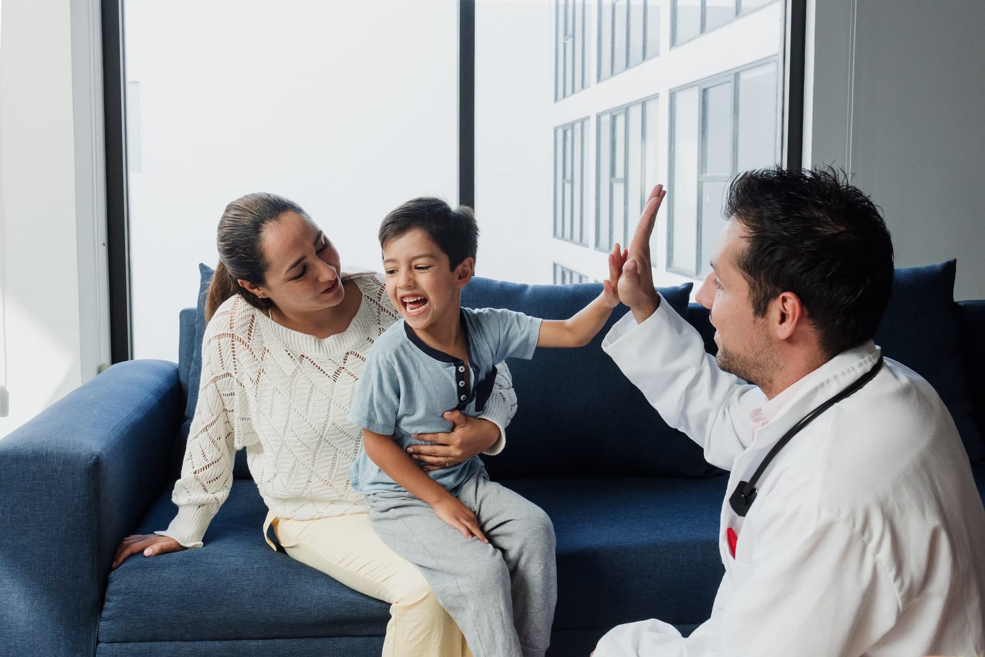 Niño feliz chocando los cinco con su pediatra durante una visita de revisión con su madre