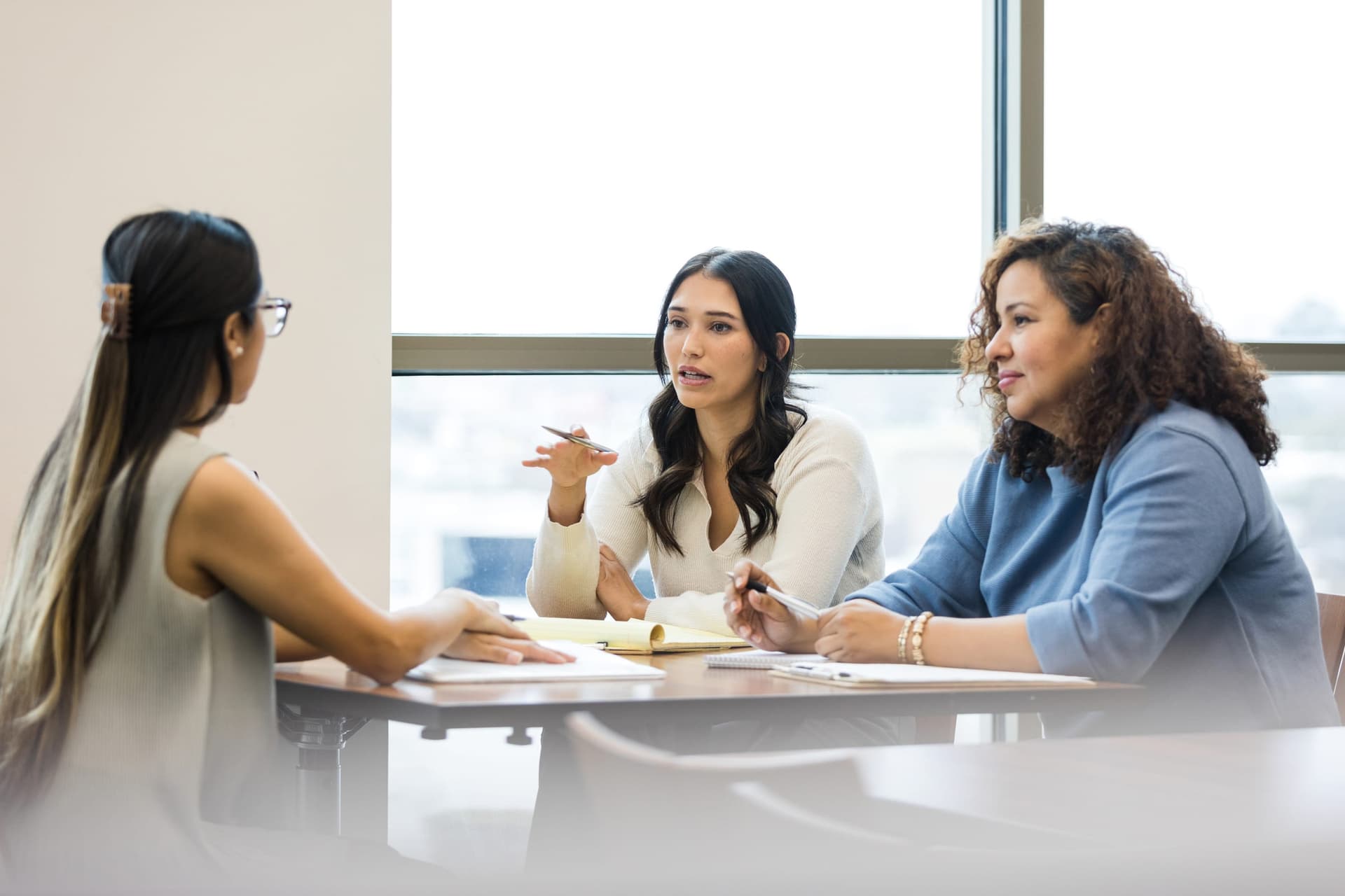 BCBA behavior analyst presenting behavior support strategies to two school staff members at a table during an IEP consultation meeting, with documentation and notepads visible
