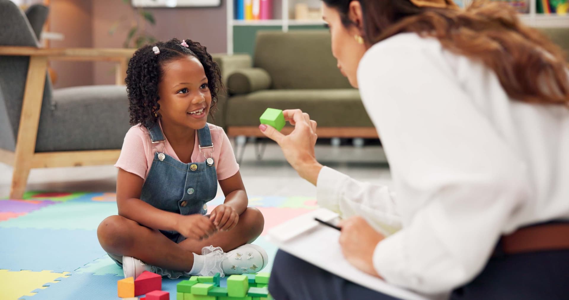 Registered behavior technician conducting an in-home ABA therapy session with a young girl holding a block while the child smiles during a discrete trial